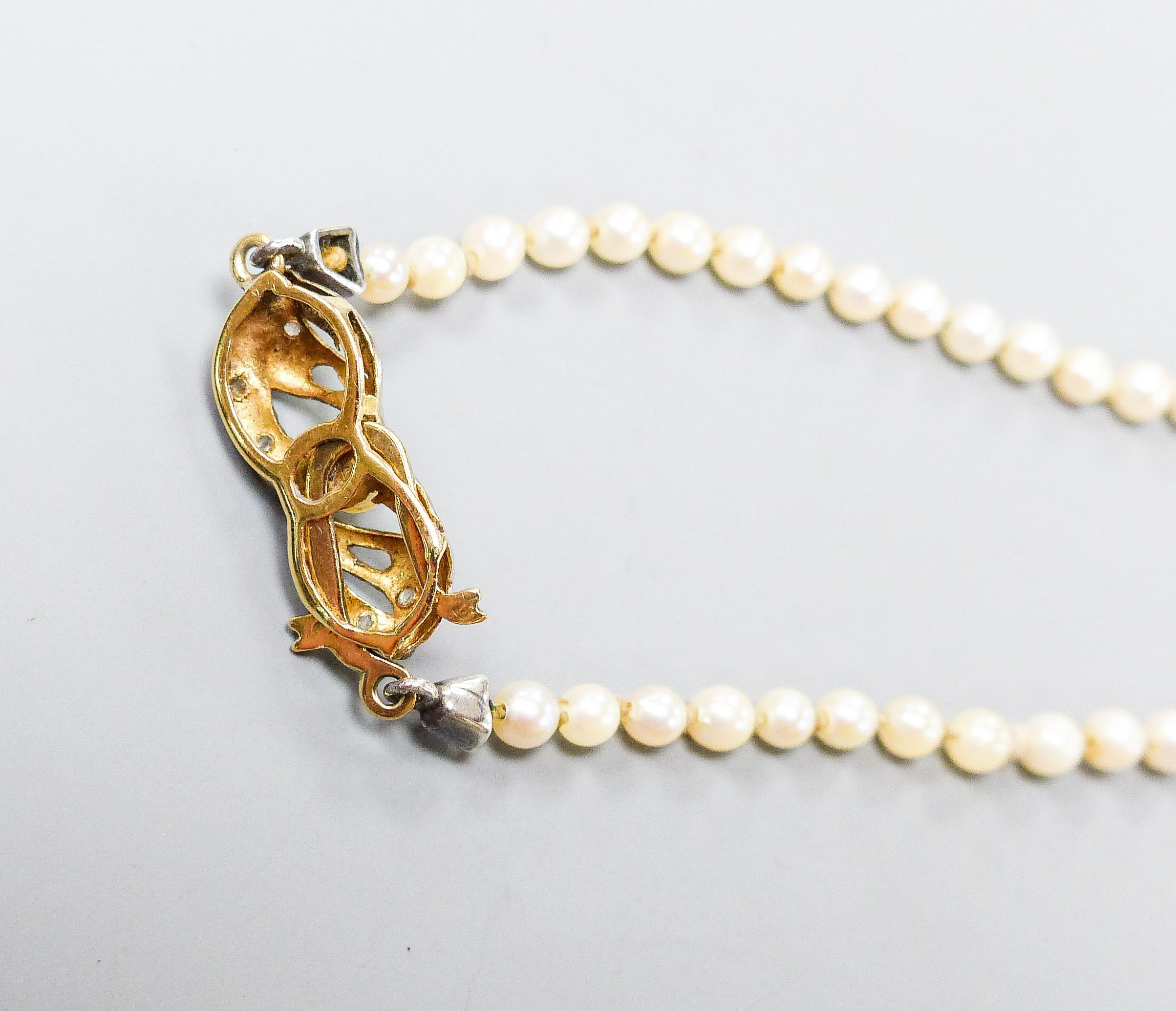 A single strand graduated cultured pearl necklace with yellow metal and gem set clasp, 49cm.